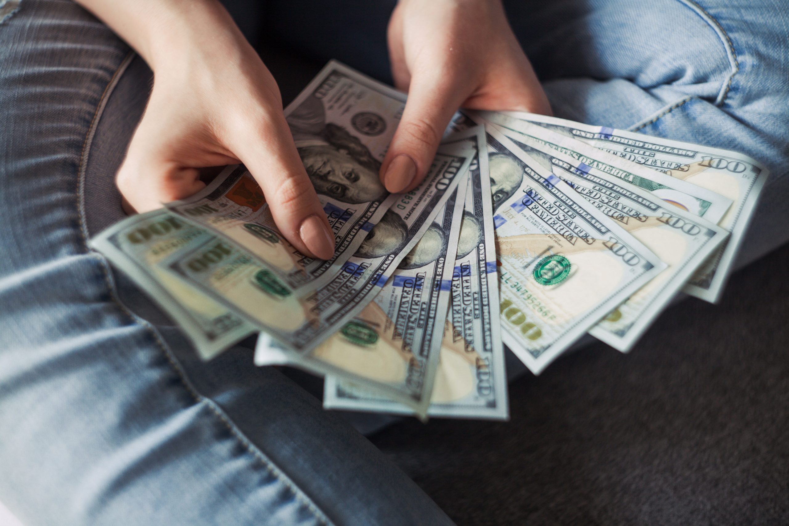 A photograph of two hands holding 100 dollar bills